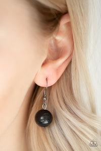 Black bead hanging from a silver fish hook earring.