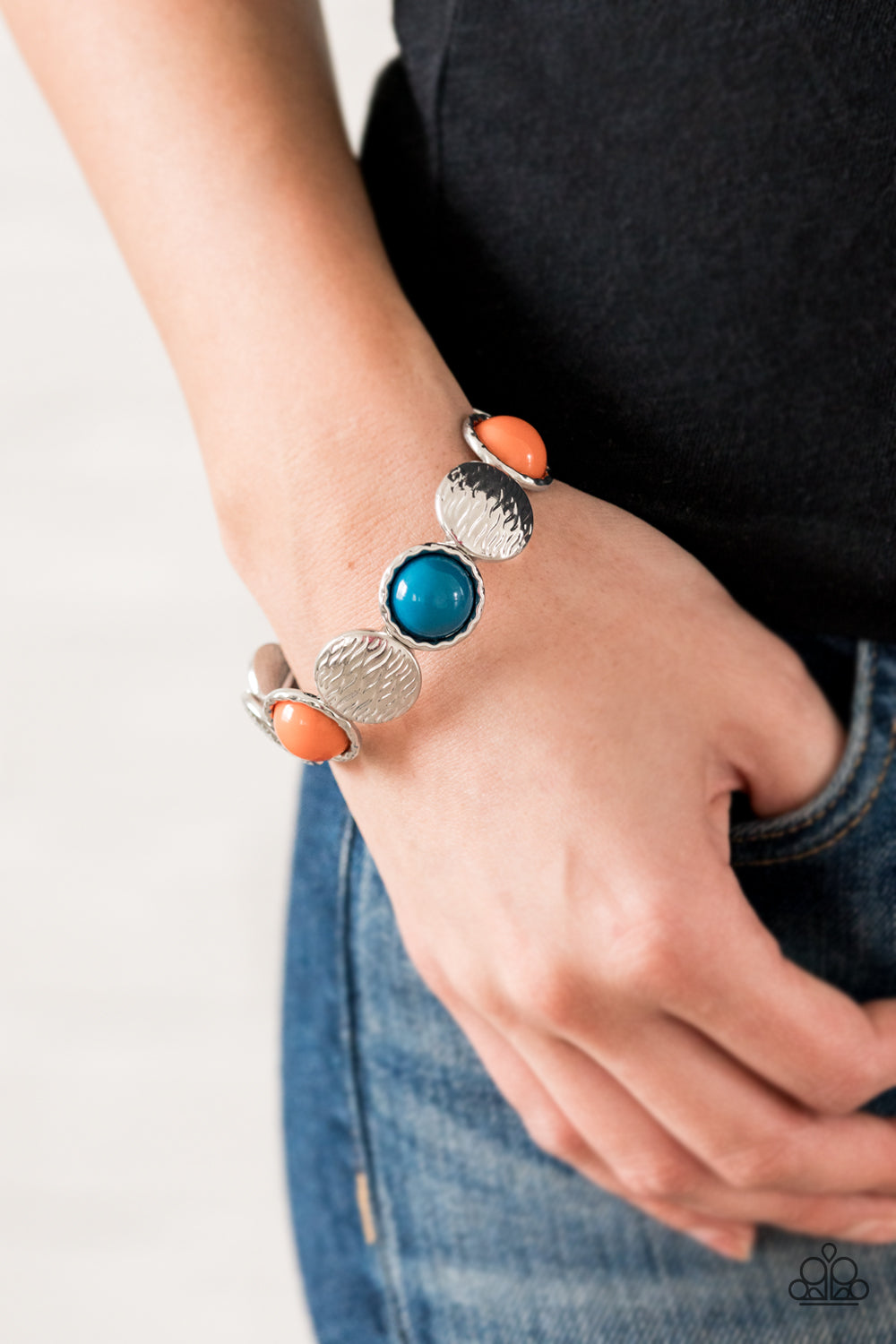 Embossed in wavy textures, shiny silver discs and bubbly orange and Mosaic Blue beaded frames are threaded along a stretchy band around the wrist, creating a colorful statement piece.