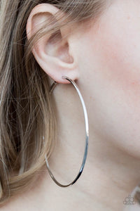 A skinny ribbon of silver curls into a bold hoop for a dramatic look. Earring attaches to a standard post fitting. Hoop measures 3” in diameter.  Sold as one pair of hoop earrings.