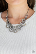 Load image into Gallery viewer, A collection of smoky crystal-like beads and hammered silver hoops dangle from the bottom of a shimmery silver chain, creating a noise-making fringe. Features an adjustable clasp closure.  Sold as one individual necklace. Includes one pair of matching earrings.
