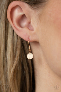 Gold disc hanging from a gold fish hook earring.