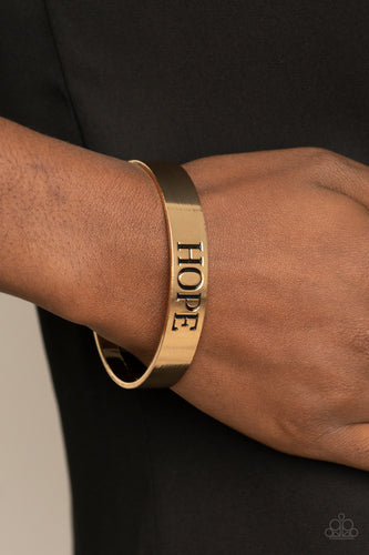 The center of a shiny gold cuff is stamped in the word, 