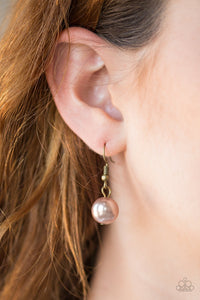 A brown pearl hanging from a  brass fish hook earring.