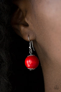 Red wooden bead dangling from a silver fish hook earring.