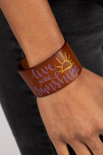 Load image into Gallery viewer, A thick band of light brown leather is stamped with the cheerful phrase, &quot;live in the sunshine,&quot; along with a radiating sun design. The purple font complements the yellow tint of the sun in an optimistic finish. Features an adjustable snap closure.  Sold as one individual bracelet.
