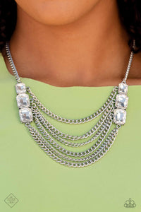 Layers of thick, silver curb chain drape across the chest, creating a fierce, industrial statement piece. Three blinding white, emerald-cut gems that gradually increase in size, are affixed to each side of the swooping chains, adding dramatic sparkle to the collision of grit and glitz. Features an adjustable clasp closure. Includes one pair of matching earrings.