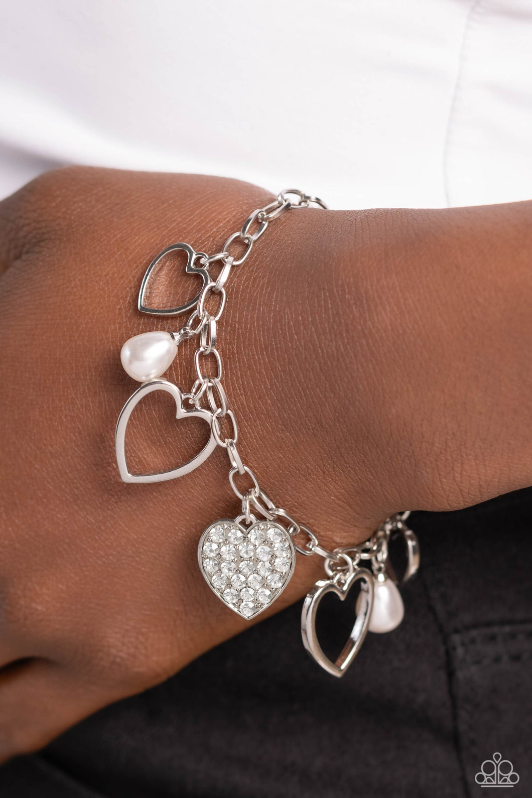 Glistening silver heart silhouettes, white potato pearls, and a white rhinestone-encrusted silver heart frame dangle from a classic silver chain link around the wrist, resulting in a romantic fringe. Features an adjustable clasp closure.  Sold as one individual bracelet